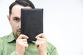 One young man hiding half of face behind a black book, looking decisively at the camera, like an analyst.