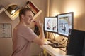 One young man, holding a pencil in front of his computer, inside of his room at his home. using a standing desk, with dual monitor