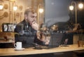 One young man, sitting in coffee shop and using his laptop while thinking and looking at street outside. Shoot thought window Royalty Free Stock Photo