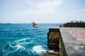 One young man or teenager enjoying the summer time and vacations outdoors at the beach jumping of a cliff to the water doing a Royalty Free Stock Photo