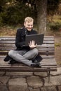 One young relaxed and smiling man, sitting casually on bench with crossed legs in public park, Royalty Free Stock Photo