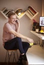 One young smiling and happy man, 20-29 years old, sitting in bar stool at his home, in his room, in front of a standing desk fill Royalty Free Stock Photo