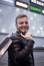 One young smiling man, looking to camera in front of a shopping mall with logos in background. carrying shopping bag on his back Royalty Free Stock Photo