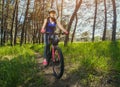 One young woman - an athlete in a helmet riding a mountain bike outside the city, on the road in a pine forest Royalty Free Stock Photo