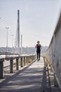One young woman, running jogging on bridge, cars in background, listening to music on headphones.