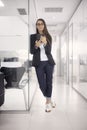One young woman standing, 20-29 years, smart casual clothes, using tablet in modern interior office. full length shot