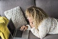 One young woman using laptop comfortably laying on the sofa at home smiling and enjoying wireless technology. House working Royalty Free Stock Photo