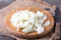 Onion slices on wood board with knife on wood table.