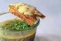 Onion soup with fresh green herbs in a glass and toasted bread with melted cheese on it against a gray background, copy space,