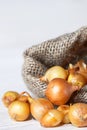 Onions in a jute bag on a wite wooden background. Spreading yellow onions.Burlap bag with onions. Vertical orientation. Royalty Free Stock Photo