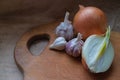 Onions, three heads of garlic on a wooden kitchen board