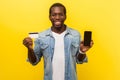 Online banking application. Portrait of happy positive man holding plastic bank card and cellphone. isolated on yellow background