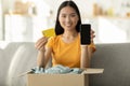 Online banking, modern shopping. Happy asian lady with cardboard box, showing phone with blank screen and credit card Royalty Free Stock Photo