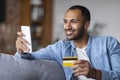 Online Banking. Smiling Black Man Using Smartphone And Holding Credit Card Royalty Free Stock Photo