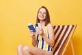 Online booking. Traveling abroad. Satisfied young woman wearing striped swimming suit sitting on deck chair using cell phone, Royalty Free Stock Photo