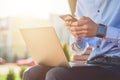 Online business. Cropped shot of a businessman using smartphone and laptop while sitting on the bench outdoors and Royalty Free Stock Photo