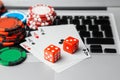 Online casino laptop. Laptop keyboard and chips with dice and playing cards on a green gaming table. Game addiction gambling Royalty Free Stock Photo