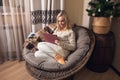Online Christmas and New year shopping or surfing the Internet or reading book. Woman sits in a round chair and looks and touches Royalty Free Stock Photo