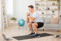 Online coach for home workout. Handsome man with fitness tracker, squats and looks at laptop Royalty Free Stock Photo