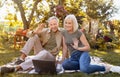 Online communication. Modern senior spouses using laptop and video calling family, sitting on picnic blanket in garden Royalty Free Stock Photo