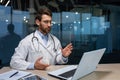 Online consultation of mature serious doctor with beard, man in medical gown using laptop for video call, explaining Royalty Free Stock Photo