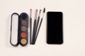 Online course of make up study. Palette of eyeshadows, cosmetics brushes and smartphone empty screen on light beige background.