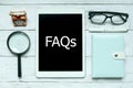 Online digital FAQs Frequently Asked Questions concept. Top view of magnifying glass,notebook,pen,glasses and tablet written with