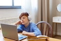 Teenager boy during an online lesson. He sits in headphones and listens to a boring lesson topic.