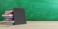 Online education concept with stack of books and digital tablet empty black screen on wooden table at green chalk board background Royalty Free Stock Photo