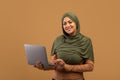 Online education for muslim women. Excited arab woman in hijab using laptop, typing on keyboard and smiling at camera Royalty Free Stock Photo