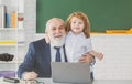 Online education. Teacher with pupil in classroom. Child with laptop. Kid is learning in class with senior mature Royalty Free Stock Photo