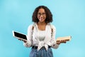 Online education vs offline studies. Black female student with backpack holding textbook and digital tablet with mockup Royalty Free Stock Photo