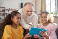 Grey-haired man in a white shirt lloking at the tablet together with two girls