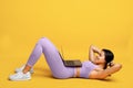 Online gym. Fit african american lady doing abs exercise sit-ups, training with laptop, exercising on yellow background Royalty Free Stock Photo