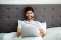 Always online. Happy arab man working on laptop distantly, sitting in bed, guy waking up and using computer, copy space Royalty Free Stock Photo