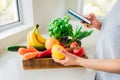 Online home delivery of fresh vegetables and fruits. Woman holding phone in one hand and lemon in other from wooden box with bio