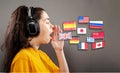 Online language learning. Portrait of a young woman wearing headphones, her hand over her open mouth. Gray background with flags Royalty Free Stock Photo