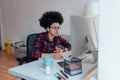 Side view of young focused afro american female student looking at computer screen and making some notes while learning