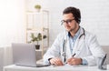 Online lessons and conferences. Doctor makes notes sitting at table with laptop