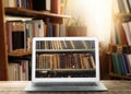 Online library. Modern laptop on wooden table and shelves with books indoors