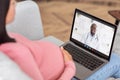 Online medical consultation. Expectant woman having video call with friendly black doctor on laptop from home Royalty Free Stock Photo