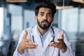 Online medical consultation. Portrait of a serious young Indian male doctor sitting in the office at the table talking Royalty Free Stock Photo