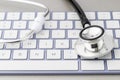 Online modern medicine or pharmacy concept. Stethoscope head on violet white keyboard on grey background