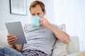 Online news and a cup of java. a handsome man drinking coffee while using his tablet at home. Royalty Free Stock Photo