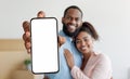 Online Offer. Happy black couple demonstrating big smartphone with blank white screen