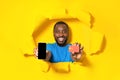 Online payments concept. Black man holding smartphone and credit card, posing through torn of yellow paper, mockup