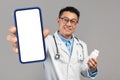 Online Pharmacy. Smiling Asian Doctor Holding Pills Bottle And Showing Blank Smartphone Royalty Free Stock Photo