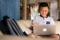 Online remote learning, distance education and homeschooling concepts. School kid Asian preteen boy in headphone using laptop