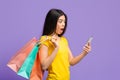 Online Sales. Shocked Asian Woman Looking At Smartphone And Holding Shopping Bags