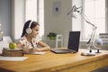 Online school training. Smart girl in headphones is studying a lesson using a laptop sitting at a table at home.